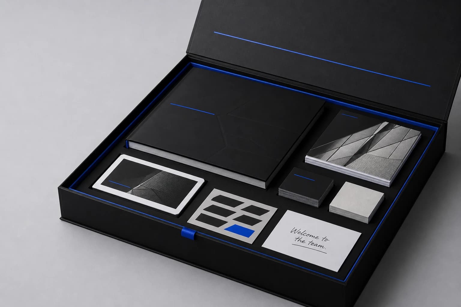 An open black client launch box containing a printed brand book, business cards, leaflets, logo pieces and a welcome note